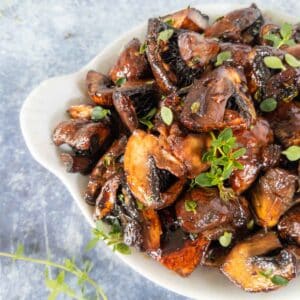 roasted mushrooms with balsamic glaze and fresh thyme leaves in a white serving dish.