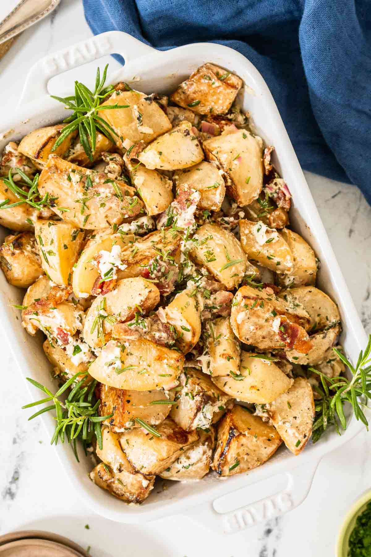 Roasted turnips topped with bacon and cheese in a white serving dish with a blue towel.