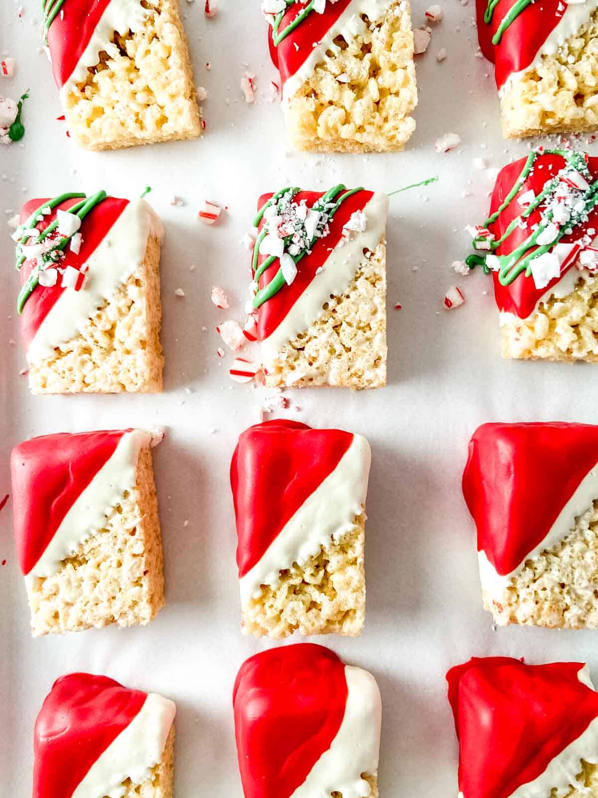 Rice cereal treats decorated with red and green chocolate and candy canes on a baking sheet.