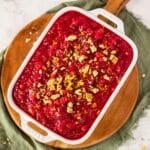 Cranberry jello salad in a white serving dish topped with chopped walnuts and orange zest.