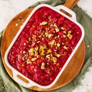 Cranberry jello salad in a white serving dish topped with chopped walnuts and orange zest.