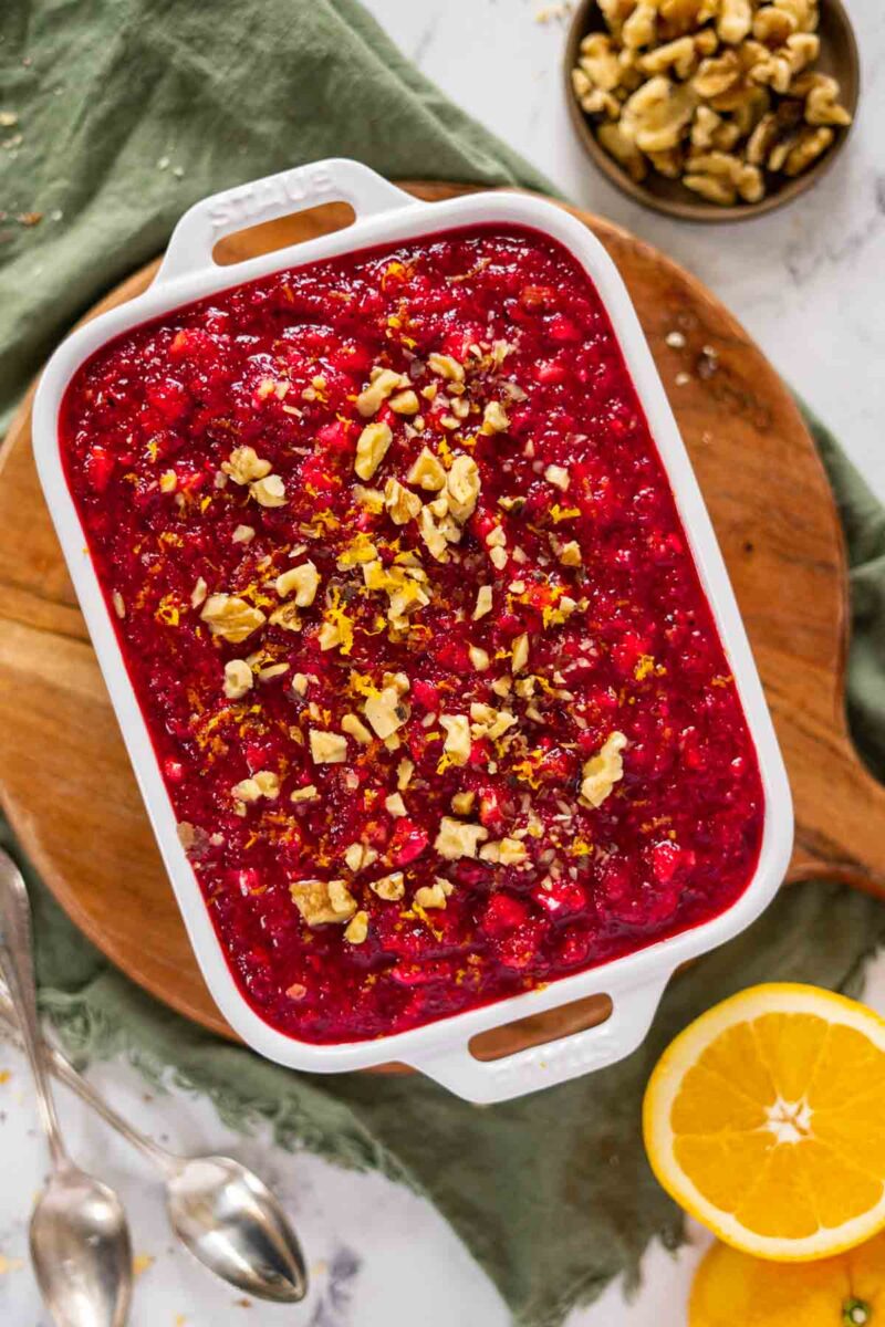 Cranberry salad in a bowl with oranges and walnuts on the side.