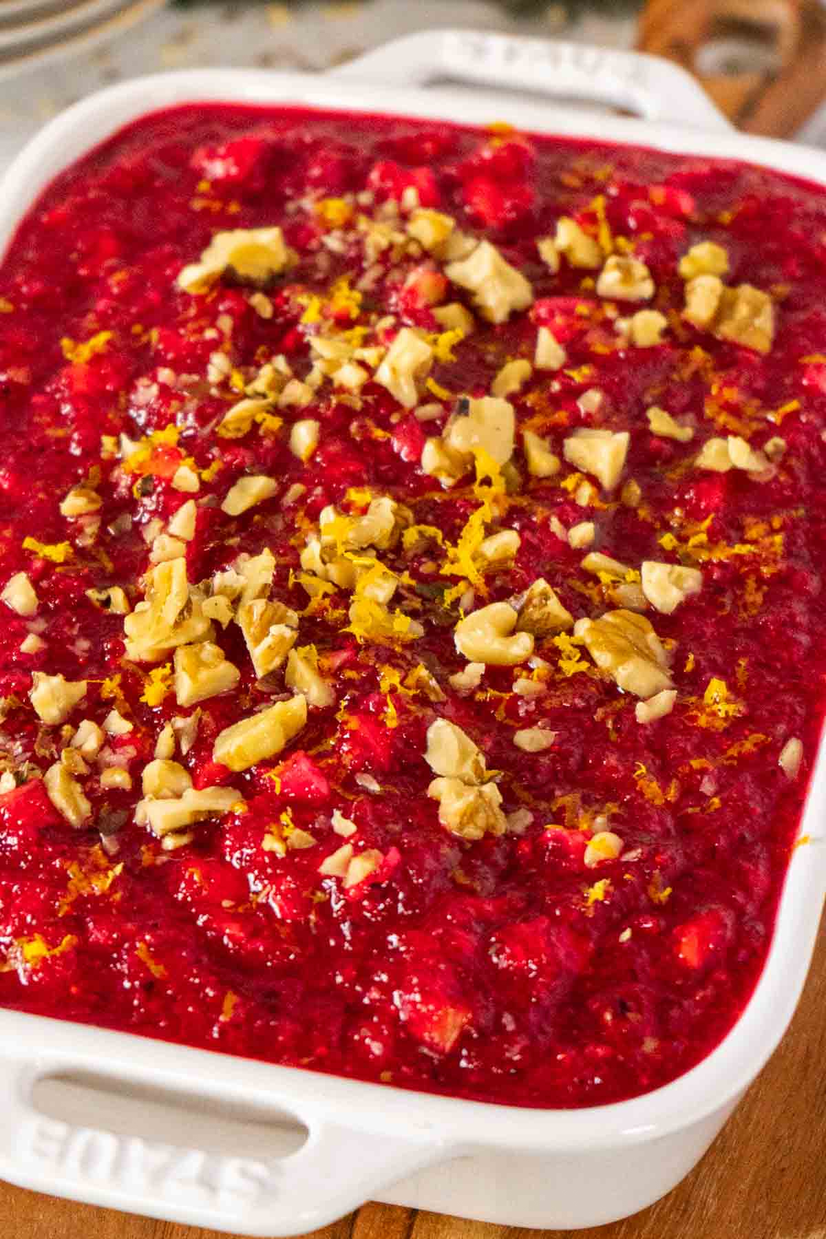 Cranberry jello salad in a white serving dish topped with chopped walnuts and orange zest.