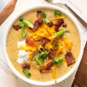 Potato soup in white bowl with bacon, onions, and cheese.