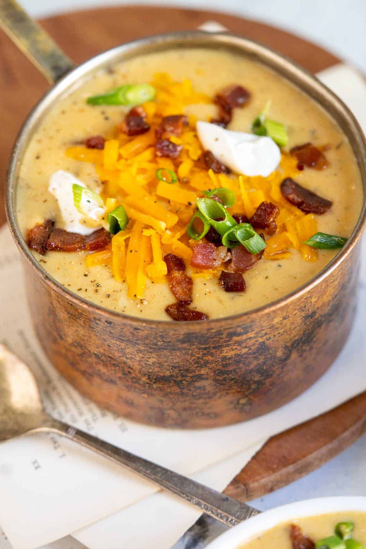 Gluten-free potato soup in a copper pot with sour cream and cheddar cheese.