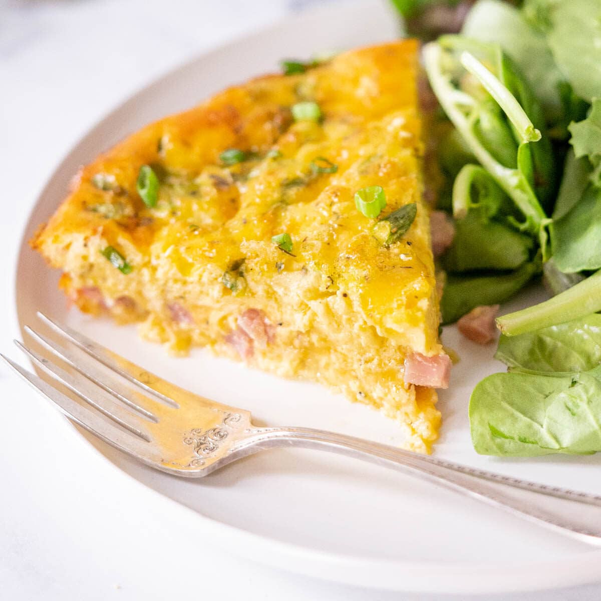 Slice of crustless quiche on a plate with a salad.