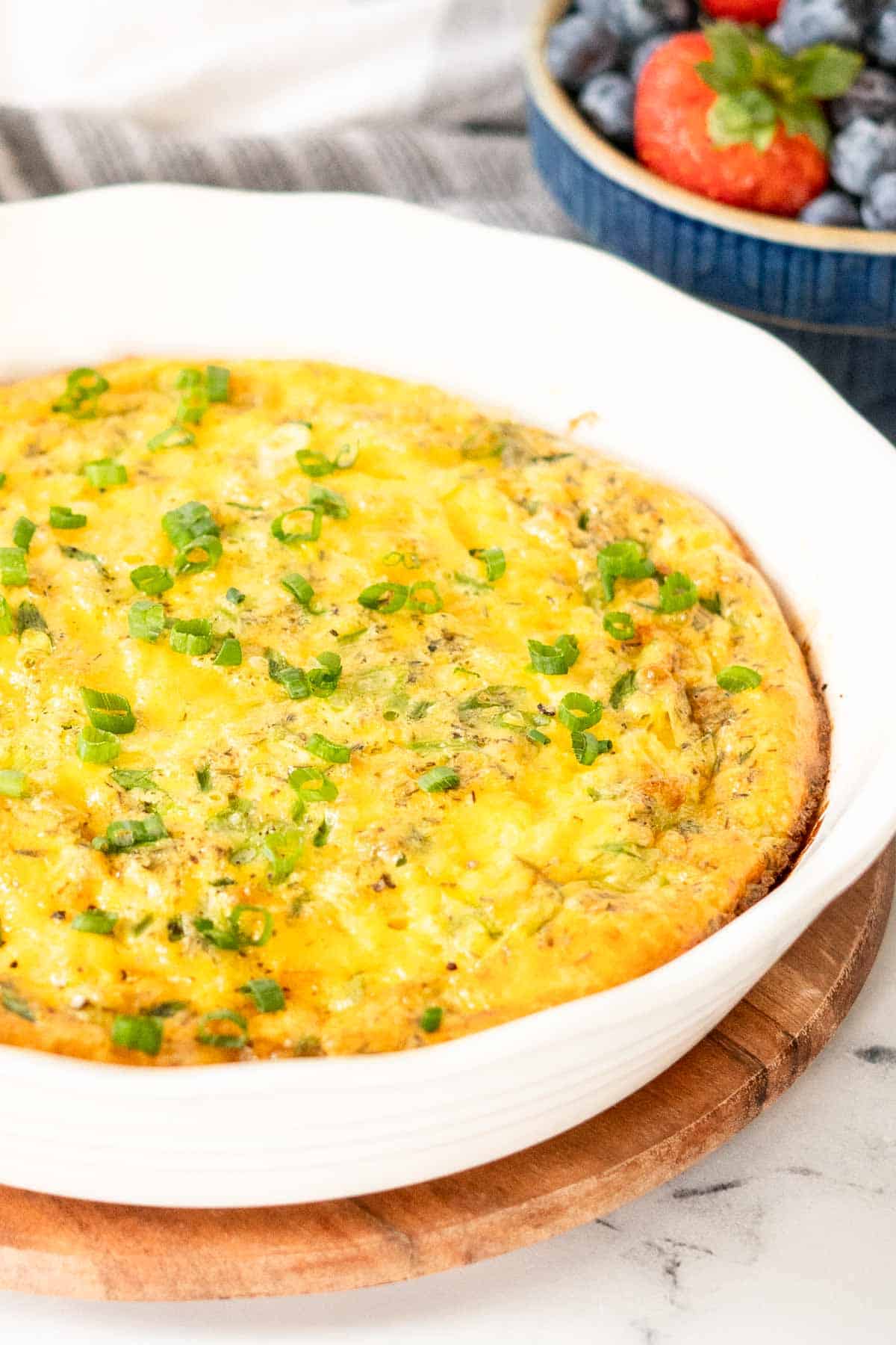 Crustless quiche in a white pie plate and topped with green onions.