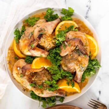 Roasted cornish hens on a plate with oranges and herbs.