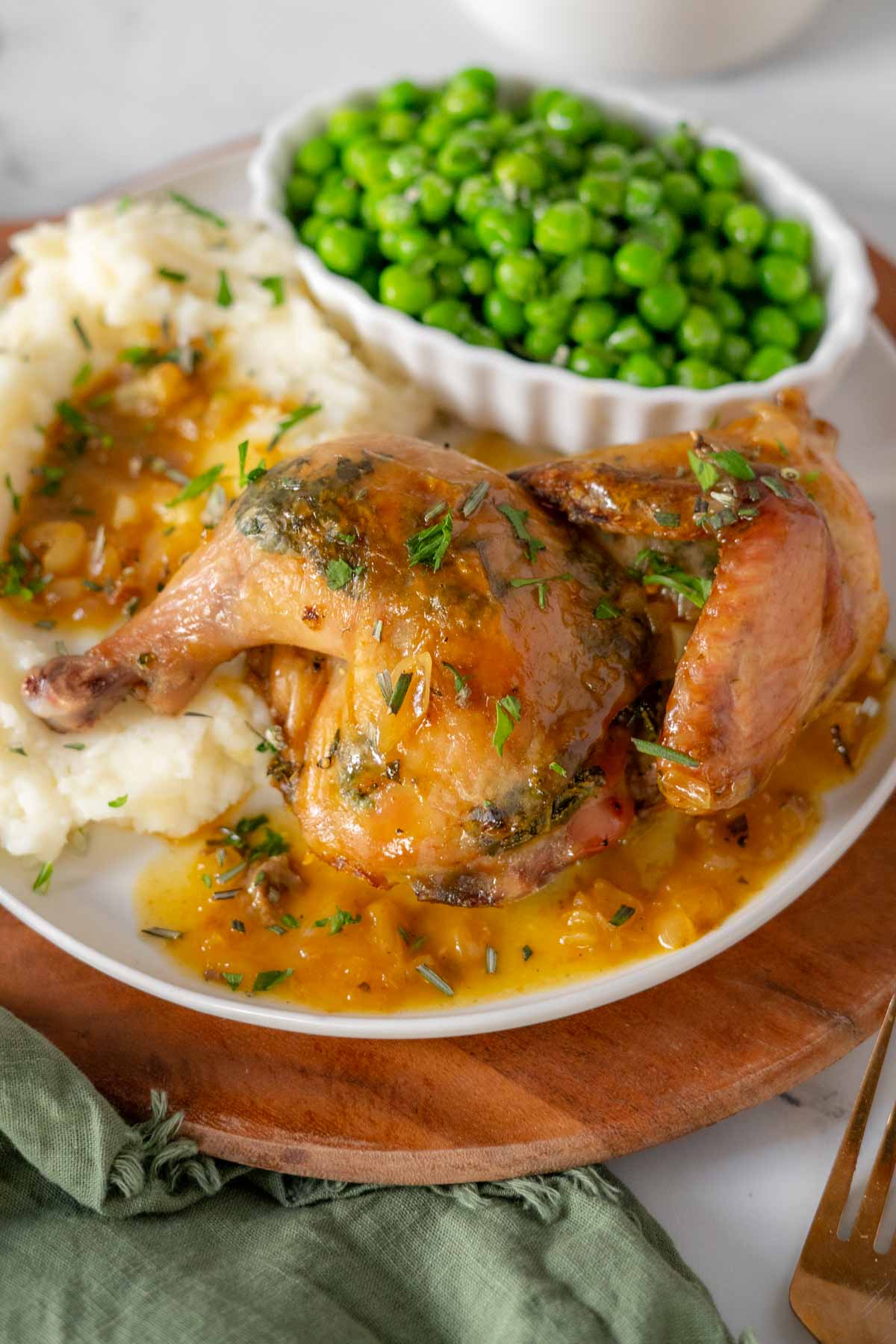 Split cornish hen on a plate with pan sauce, potatoes and peas.