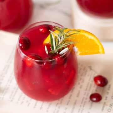 Cocktail glass with an orange slice, fresh cranberries, and a rosemary sprig garnish.