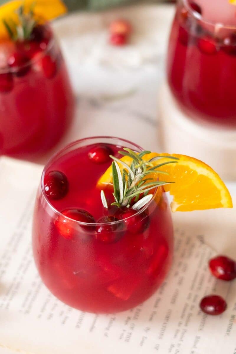 Cocktail glass with an orange slice, fresh cranberries, and a rosemary sprig garnish.