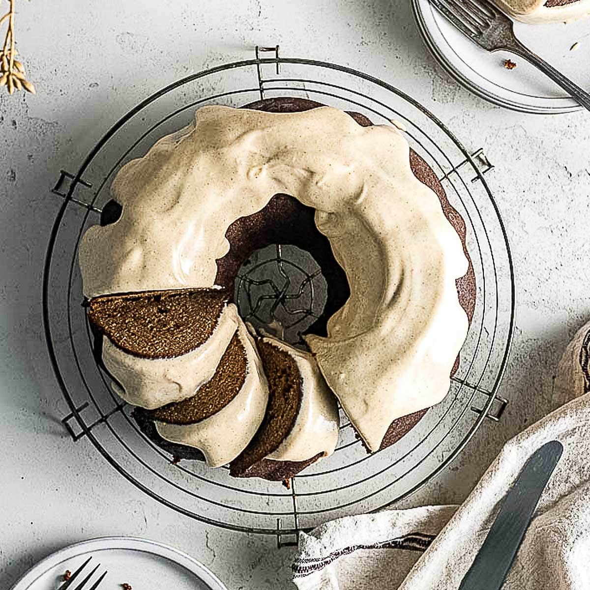 A round bundt cake, perfect for Gluten-Free Christmas Desserts, with light brown icing sits on a wire cooling rack. Three slices have been cut and are partially separated from the rest of the cake.