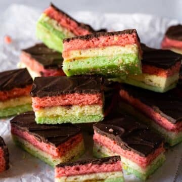 Italian rainbow cookies stacked on a piece of parchment.