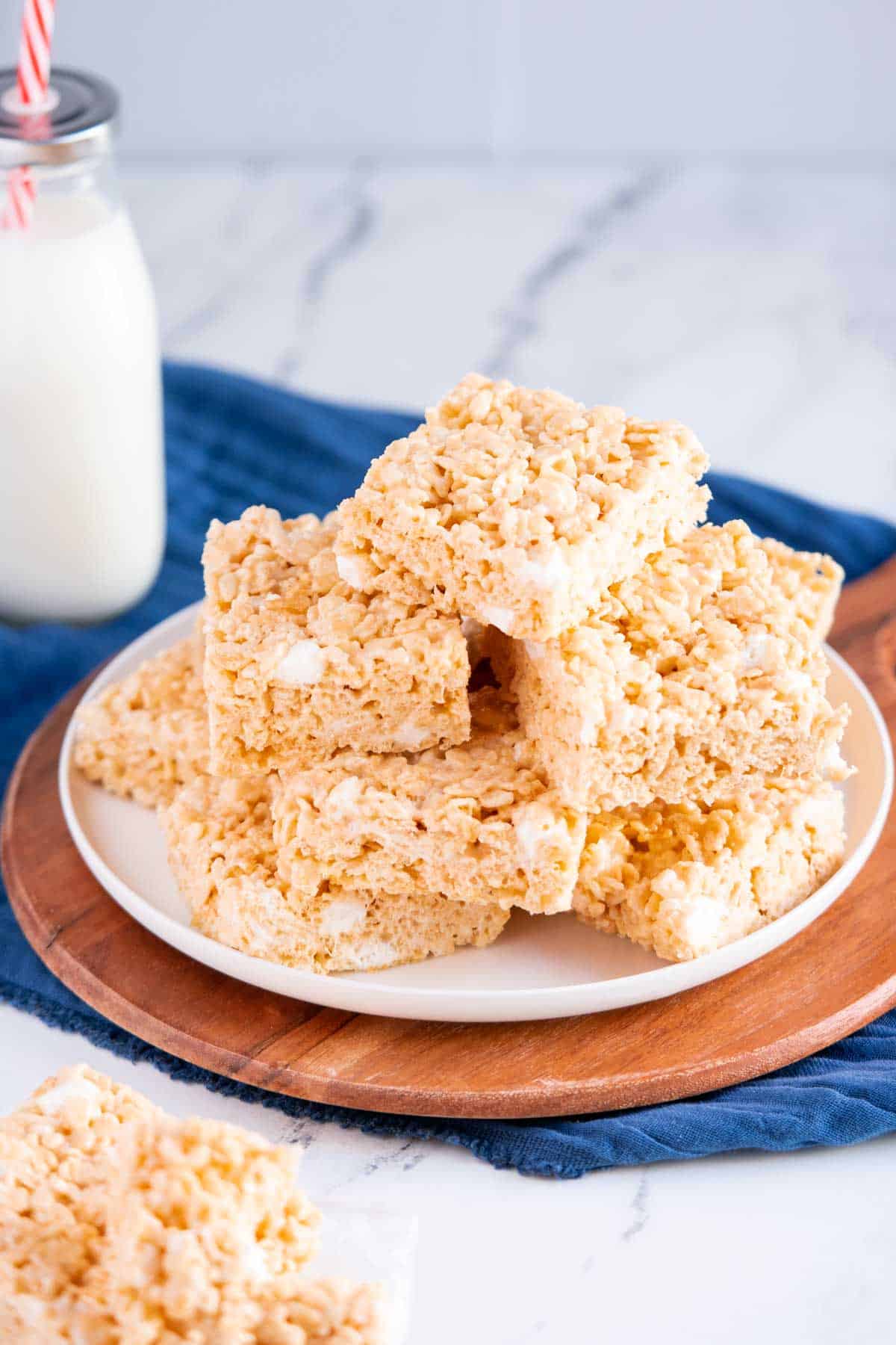 Stock of marshmallow rice krispies treats on a plate with a bottle of milk.