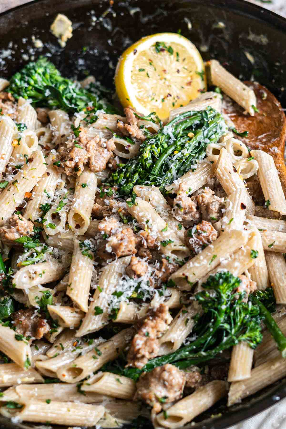 Penne pasta with broccolini, sausage, and parmesan cheese in a skillet.