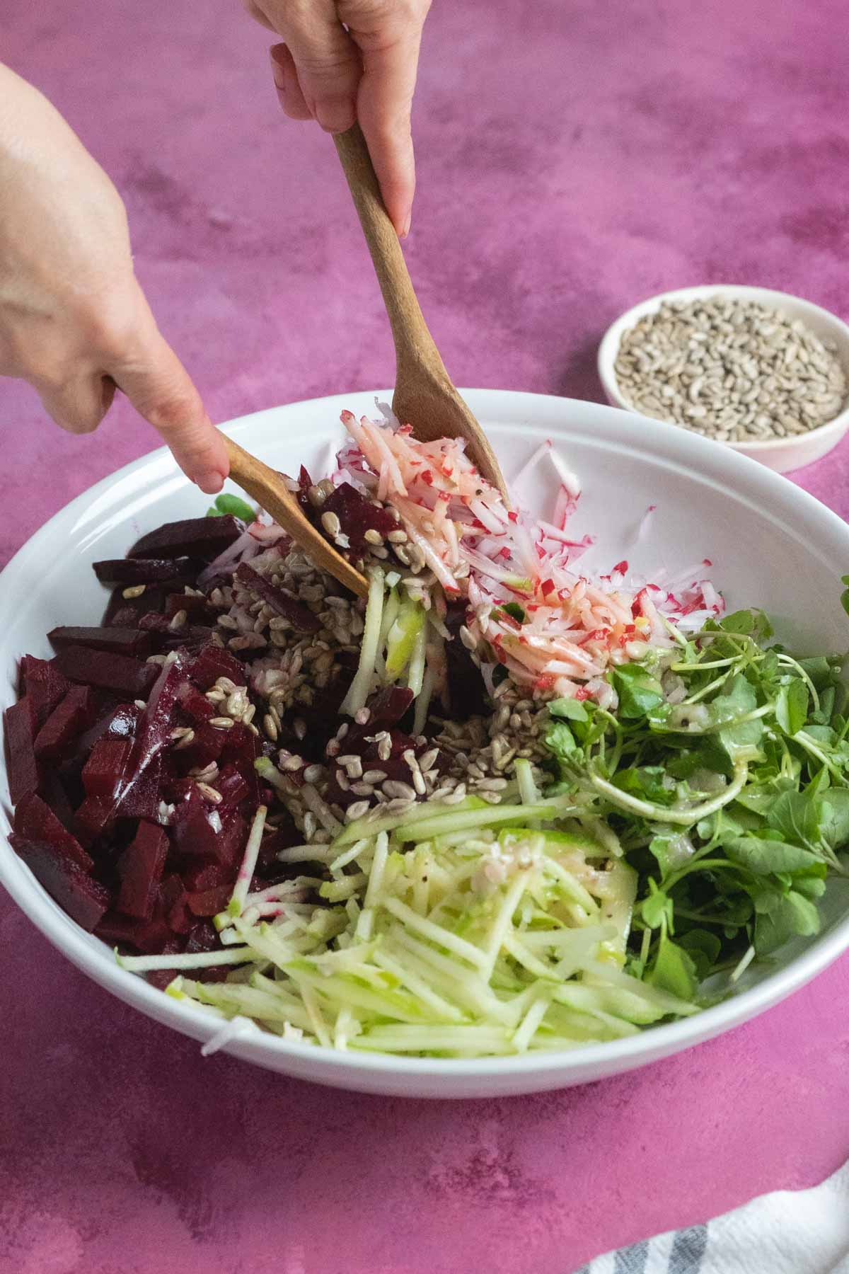Person using tongs to mix salad ingredients.