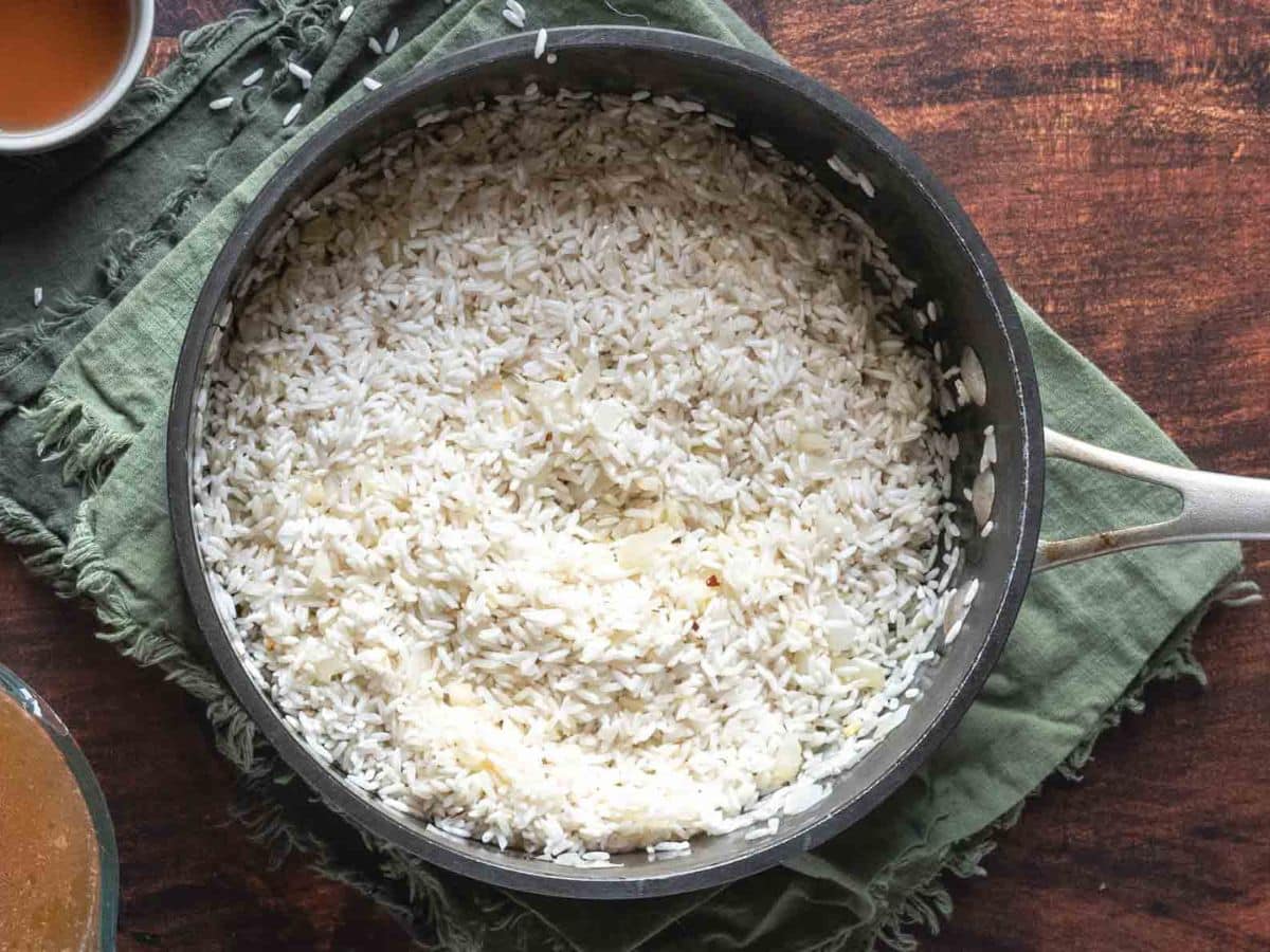 A pot of rice as it is toasted rests on a green cloth, sitting elegantly on a wooden surface.