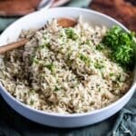 Rice with green herbs in a serving bowl with a wooden spoon.