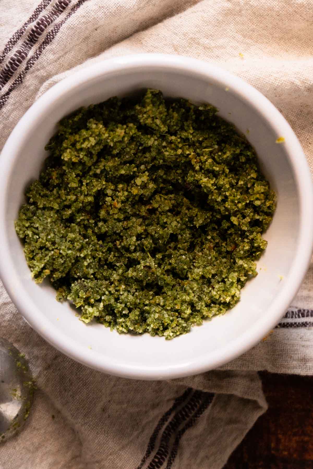 A white bowl filled with a coarse, salt dry bine mixture sits on a beige cloth with dark stripes-perfect for drizzling over roast vegetables or adding flavor after you learn how to dry brine a turkey.