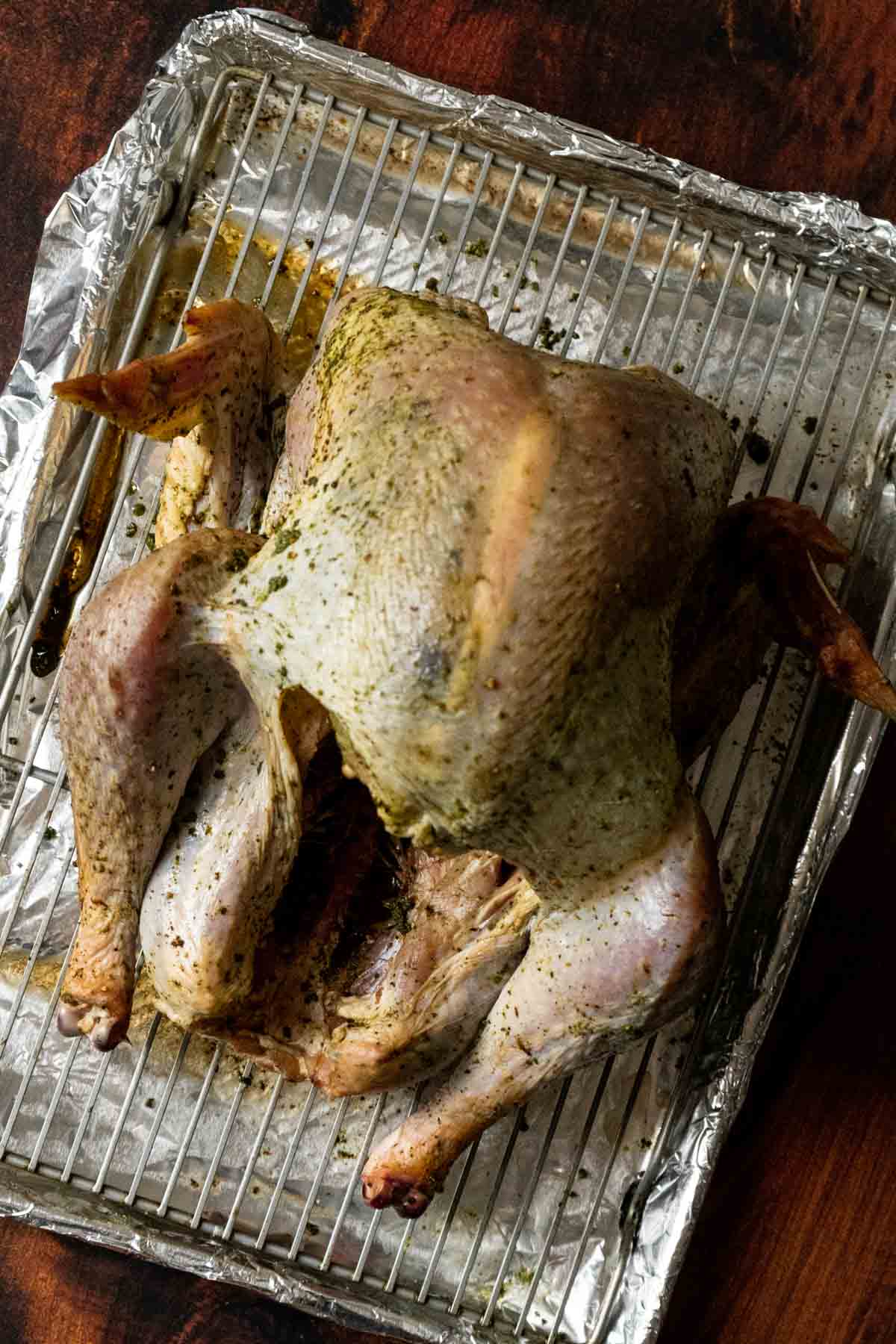 A whole seasoned turkey, prepared using the how to dry brine a turkey method, rests on a wire rack over a foil-lined baking sheet.