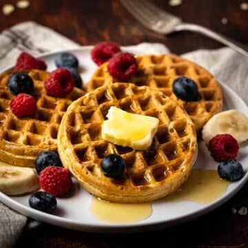 Waffles on a plate with butter and fresh berries.