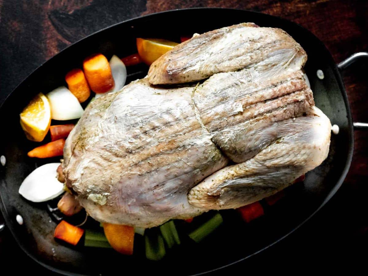 A raw, whole duck is placed in a roasting pan on a bed of chopped vegetables-carrots, onions, and celery-prepared just as you would for a classic roast turkey.
