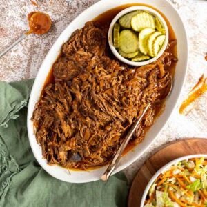 BBQ shredded beef on a serving platter with pickles.