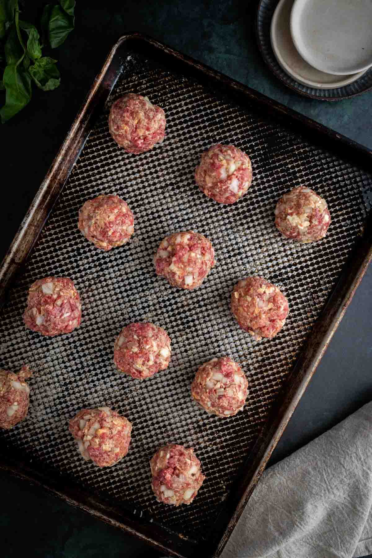 Meatballs arranged on a baking sheet ready for bake, is placed on the countertop.