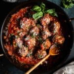 Meatballs in spaghetti sauce in a pan with wooden spoon.
