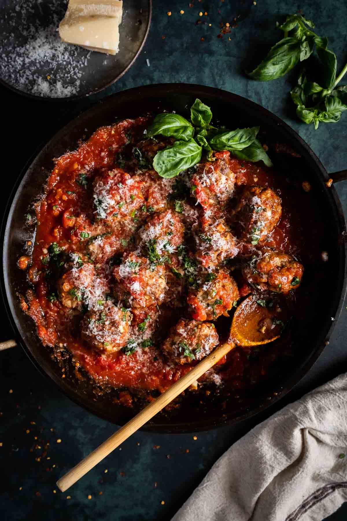 Meatballs in spaghetti sauce in a pan with wooden spoon.