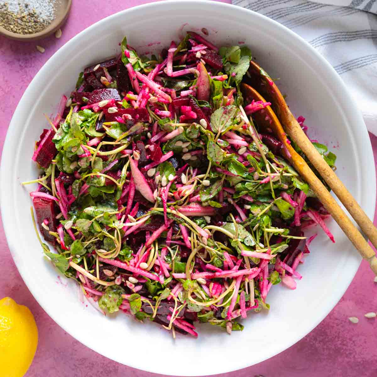 Salads with beets and apples in a bowl with wooden serving spoons.