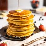 Syrup being poured on a stack of cornmeal pancakes.