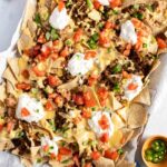 Beef nachos on a sheet pan topped with sour cream and tomatoes.