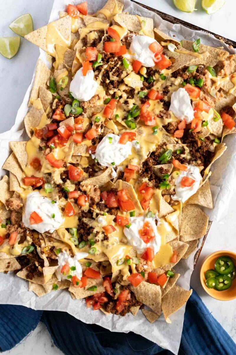 Beef nachos on a sheet pan topped with sour cream and tomatoes.