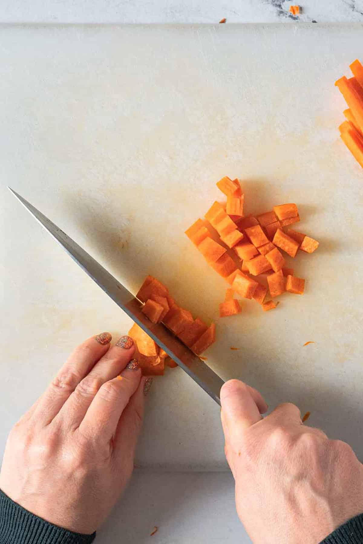 Person chopping matchstick carrots into little dices.