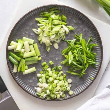 Green onions cut in different ways on a plate.
