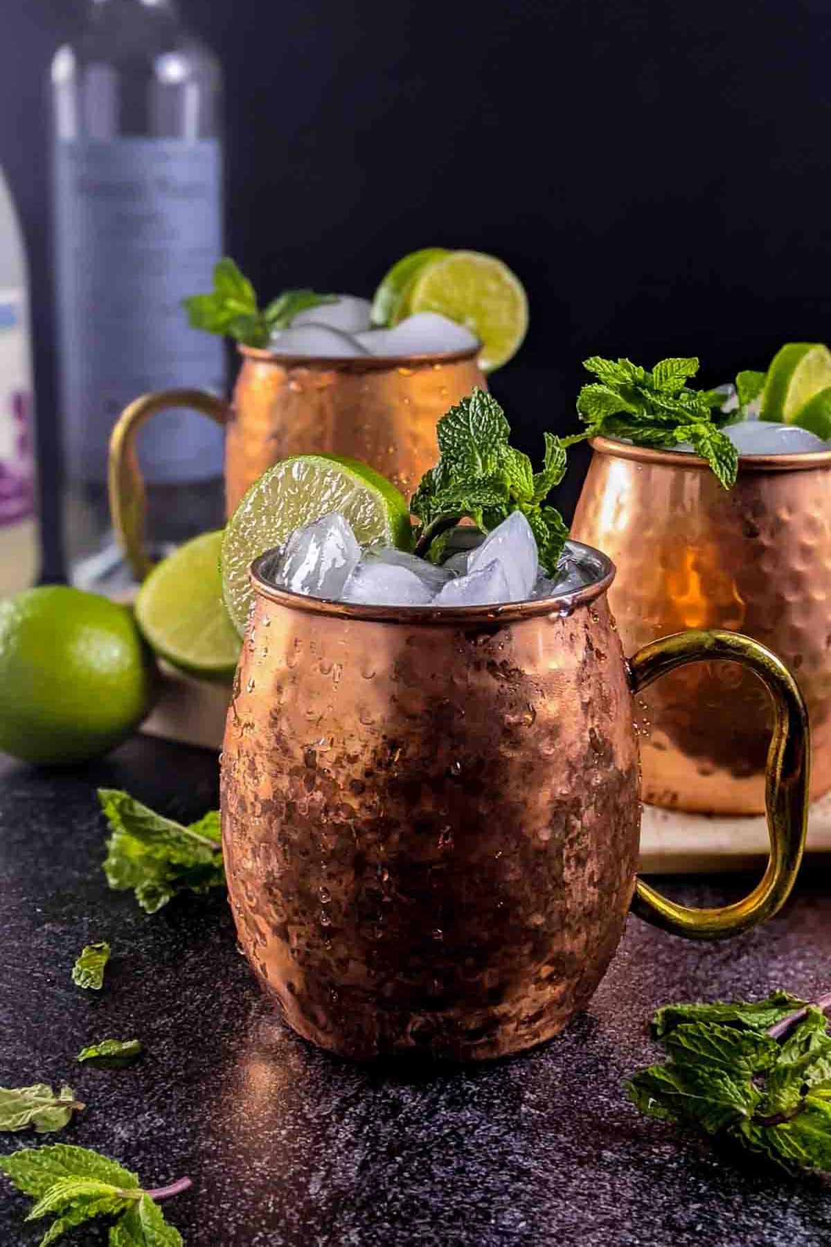 Cocktails in a copper mugs with a bottle of mezcal in the background.