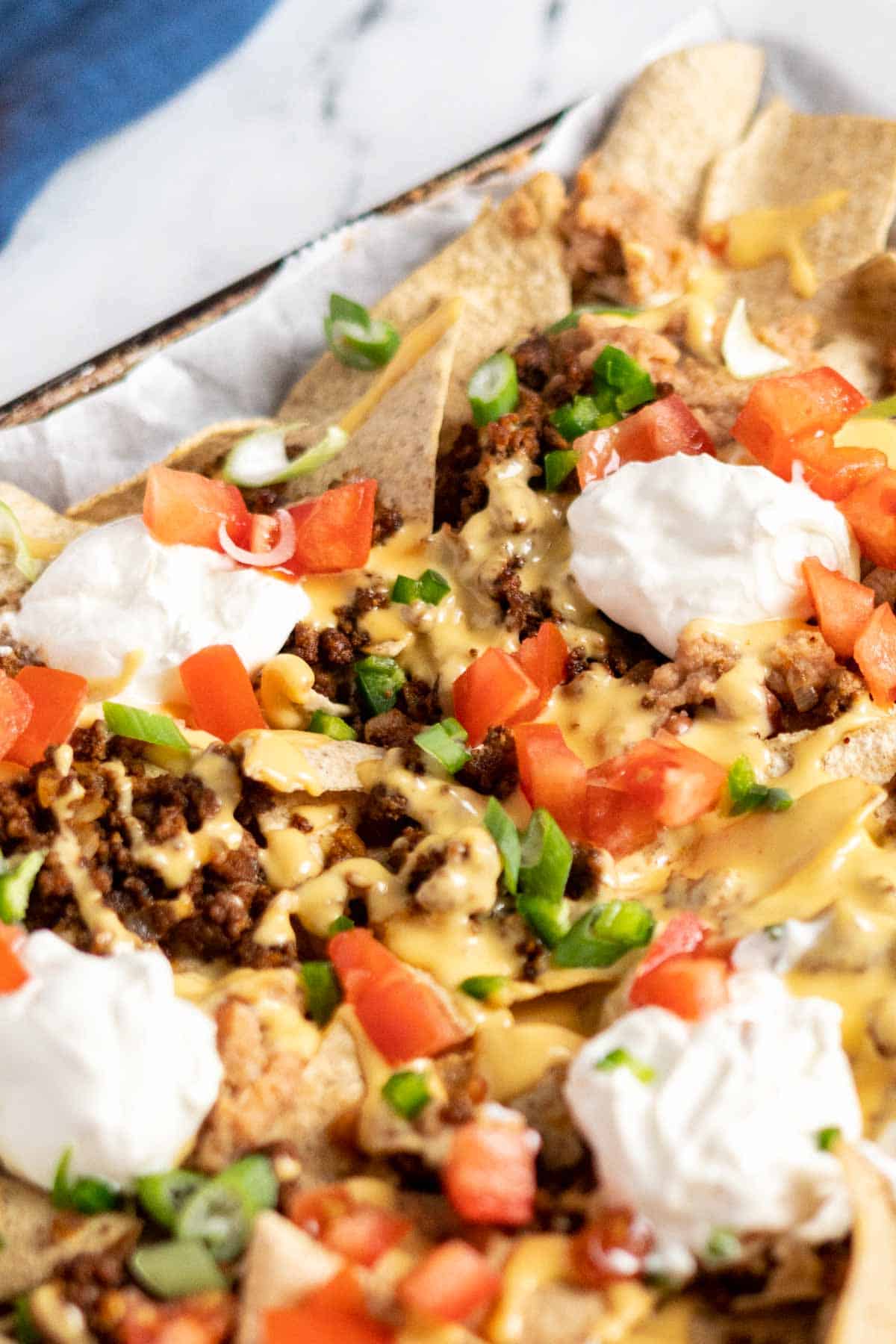 Nachos topped with sour cream, tomatoes, and green onion.