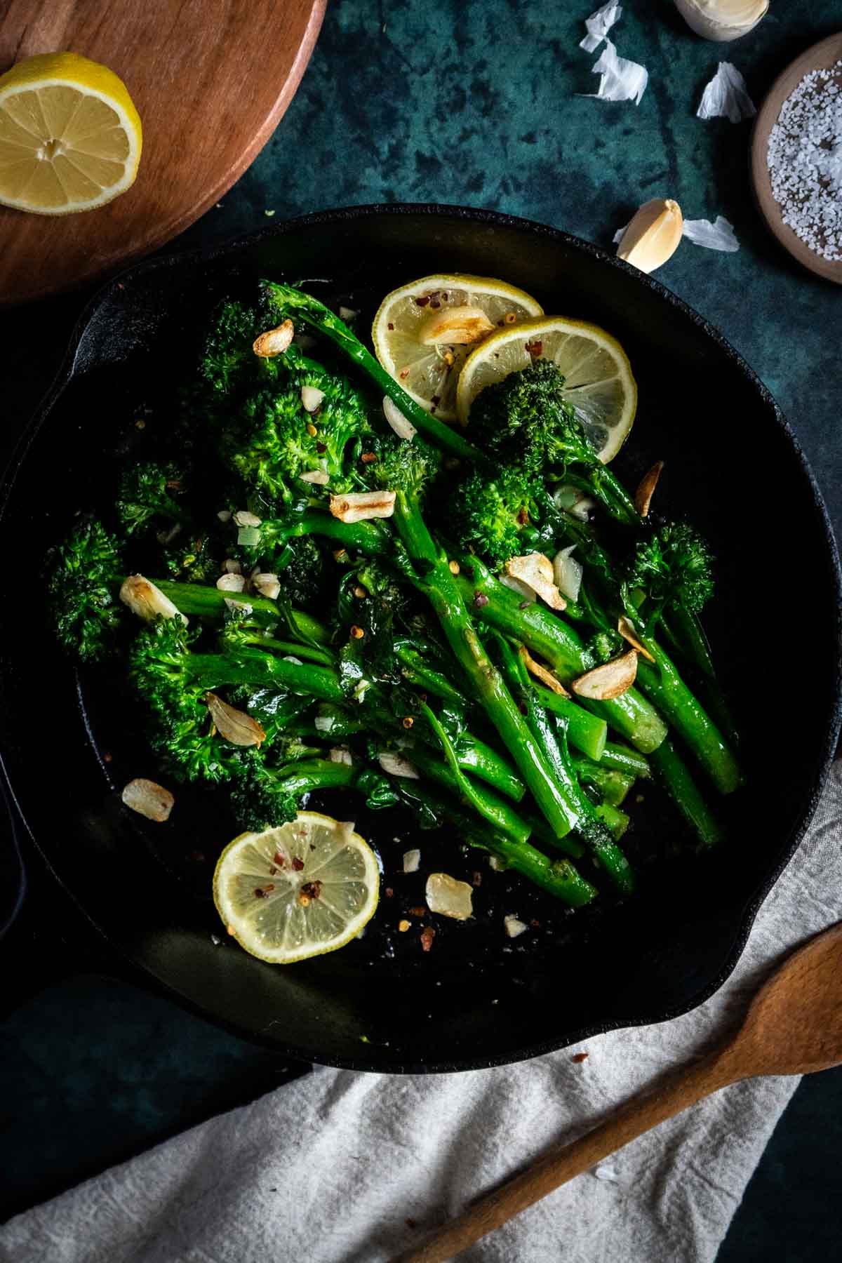 Pan of broccolini on counter with napkin and wooden spoon.
