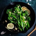 Broccolini in a cast iron pan with lemon slices and garlic.