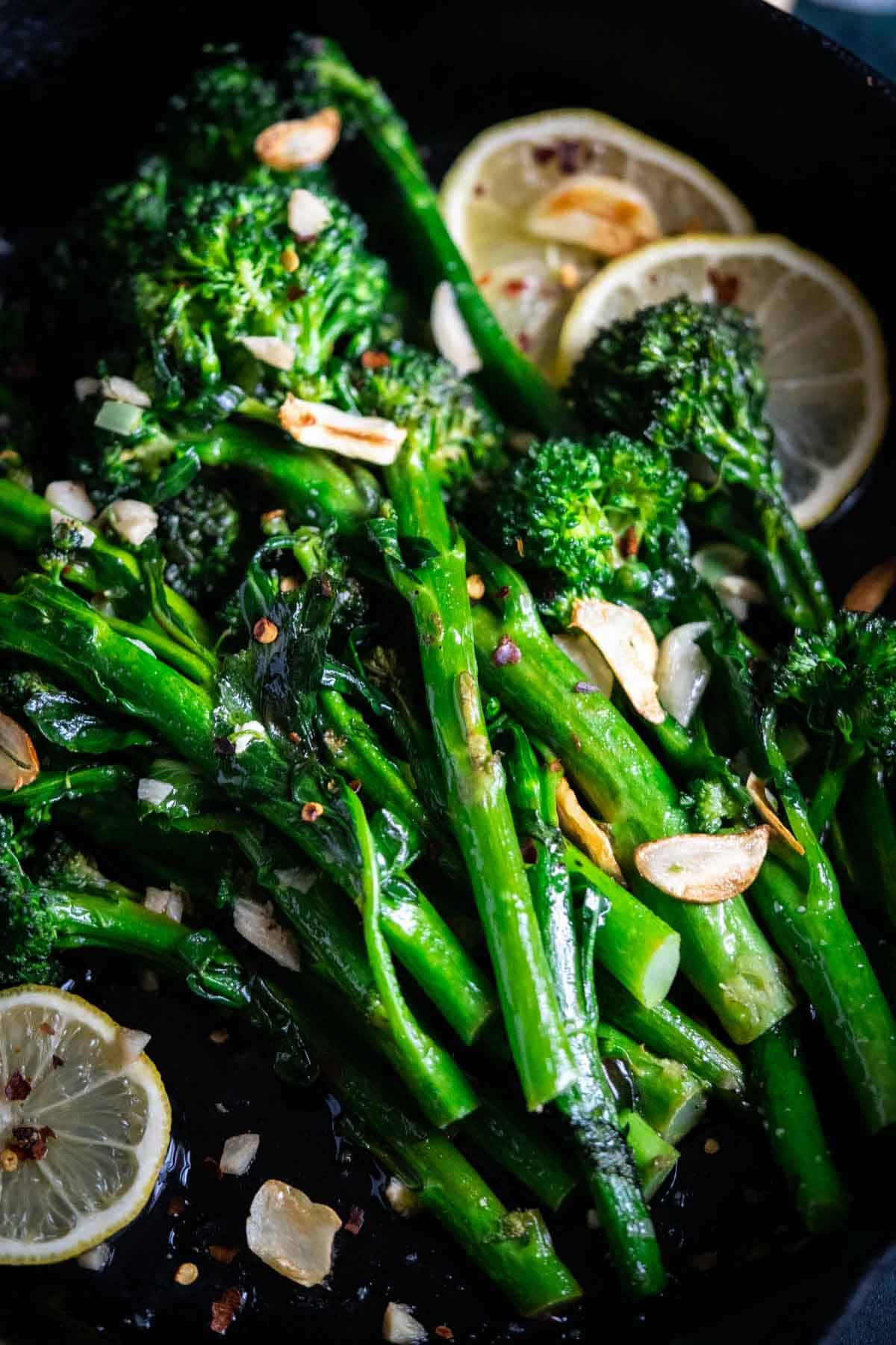 Broccolini in a cast iron pan with lemon slices and garlic.