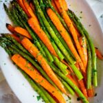 Cooked asparagus and carrots on a plate with fresh herbs.