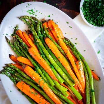 Roasted asparagus and carrots on a serving platter with fresh herbs.