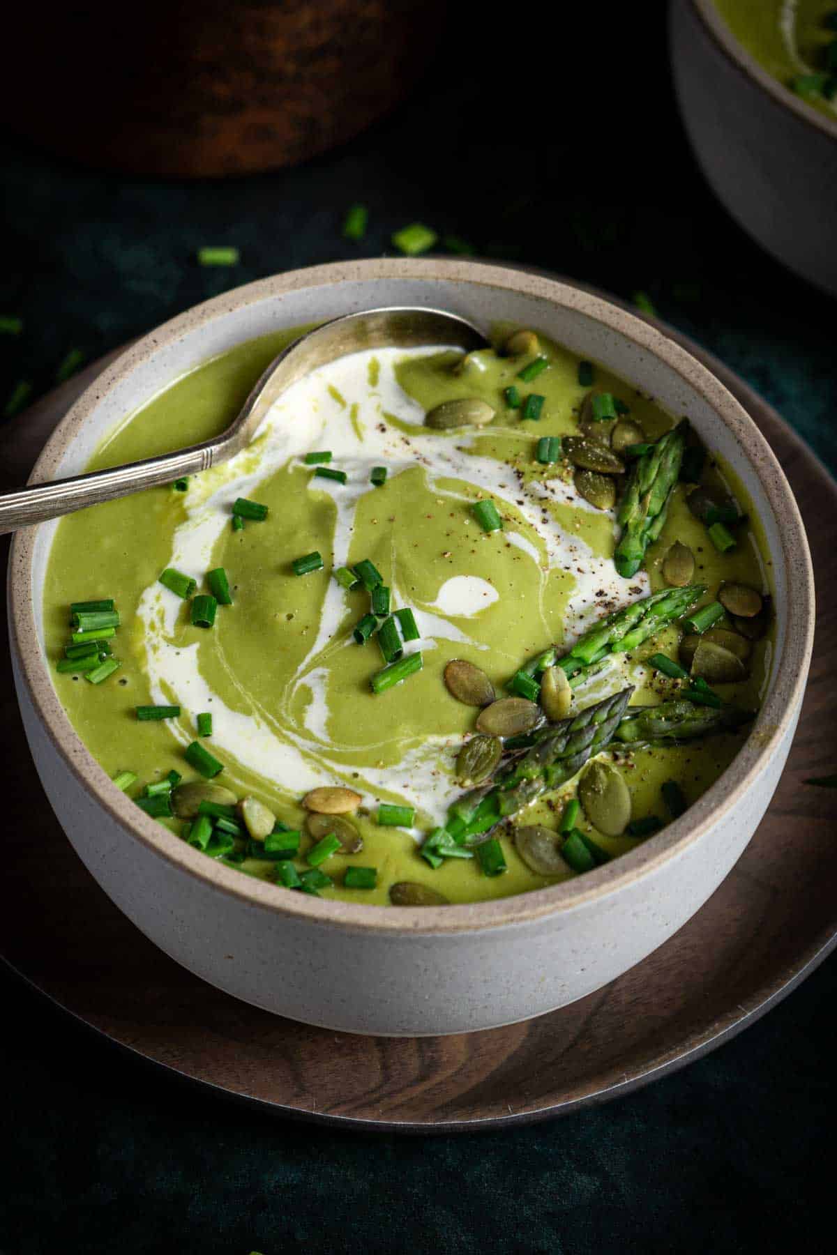 Green soup topped with chives in a bowl with a spoon.