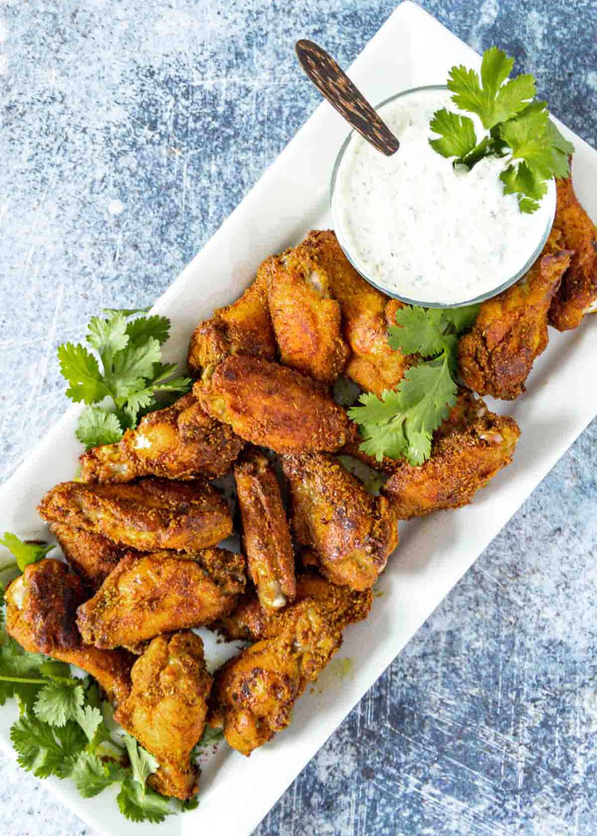 Crispy chicken wings on a plate with a dipping sauce.