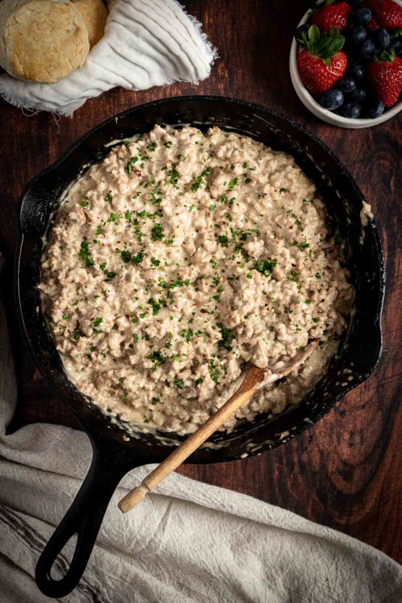 Sausage gravy in a skillet with a wooden spoon and a towel.