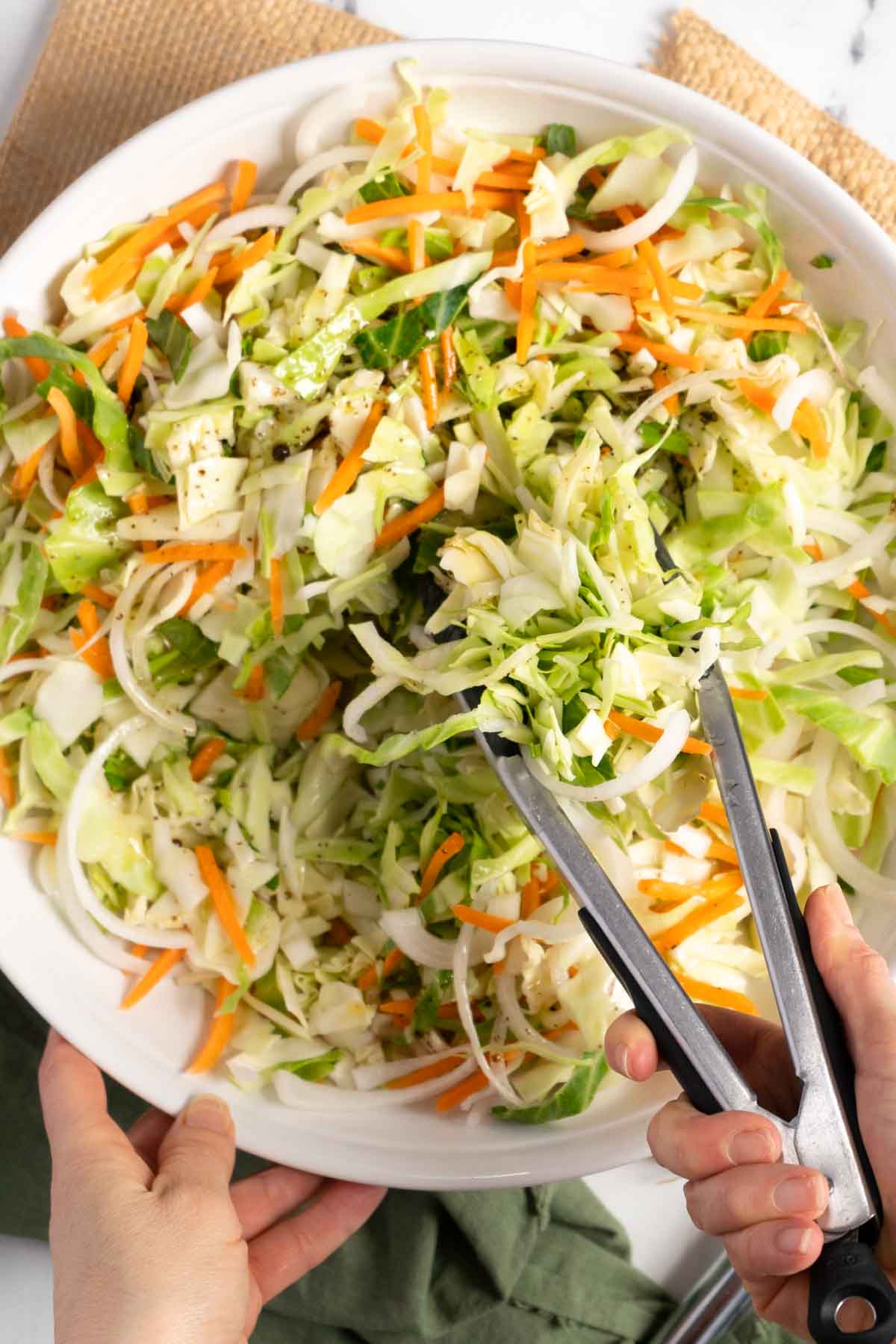 Person tossing the coleslaw with tongs.