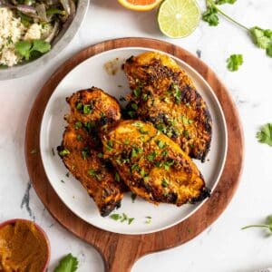 Chicken on a plate with asado marinade and cilantro leaves.