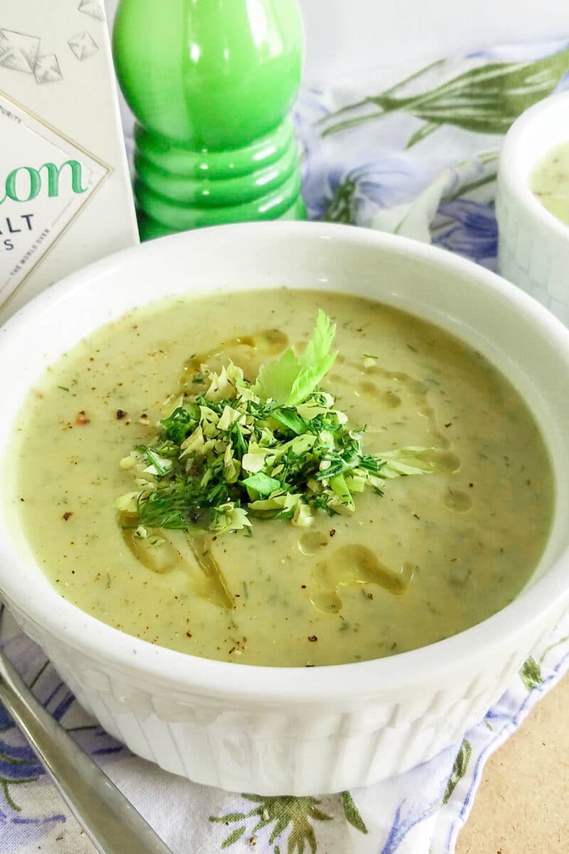 Soup in a white bowl with celery leaves.