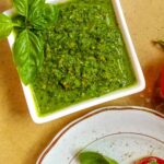Basil pesto in bowl with a plate of tomatoes.